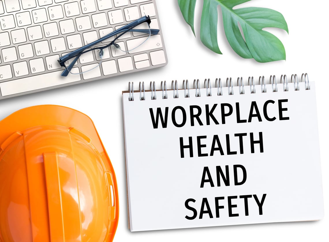 Orange safety helmet with words workplace health and safety write in notebook.