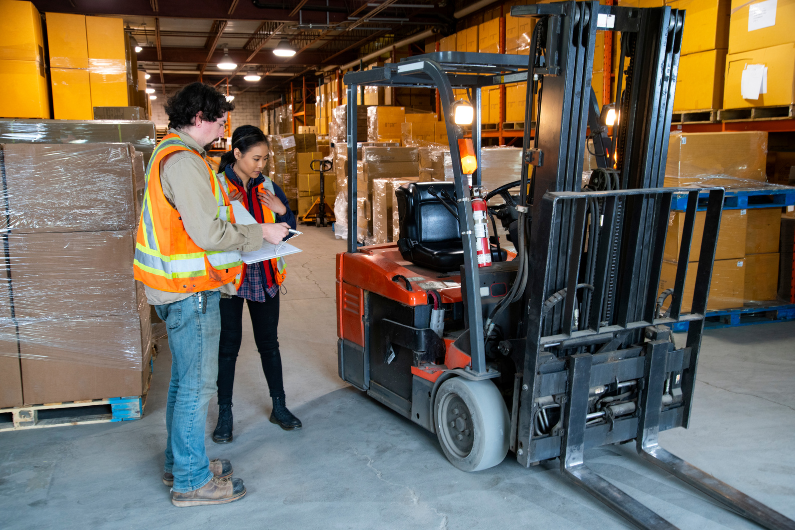 An industrial warehouse workplace safety topic.  A safety supervisor or manager training a new employee on forklift safety.